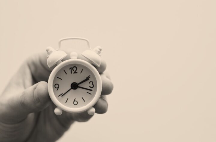 A hand holding up a tiny alarm clock